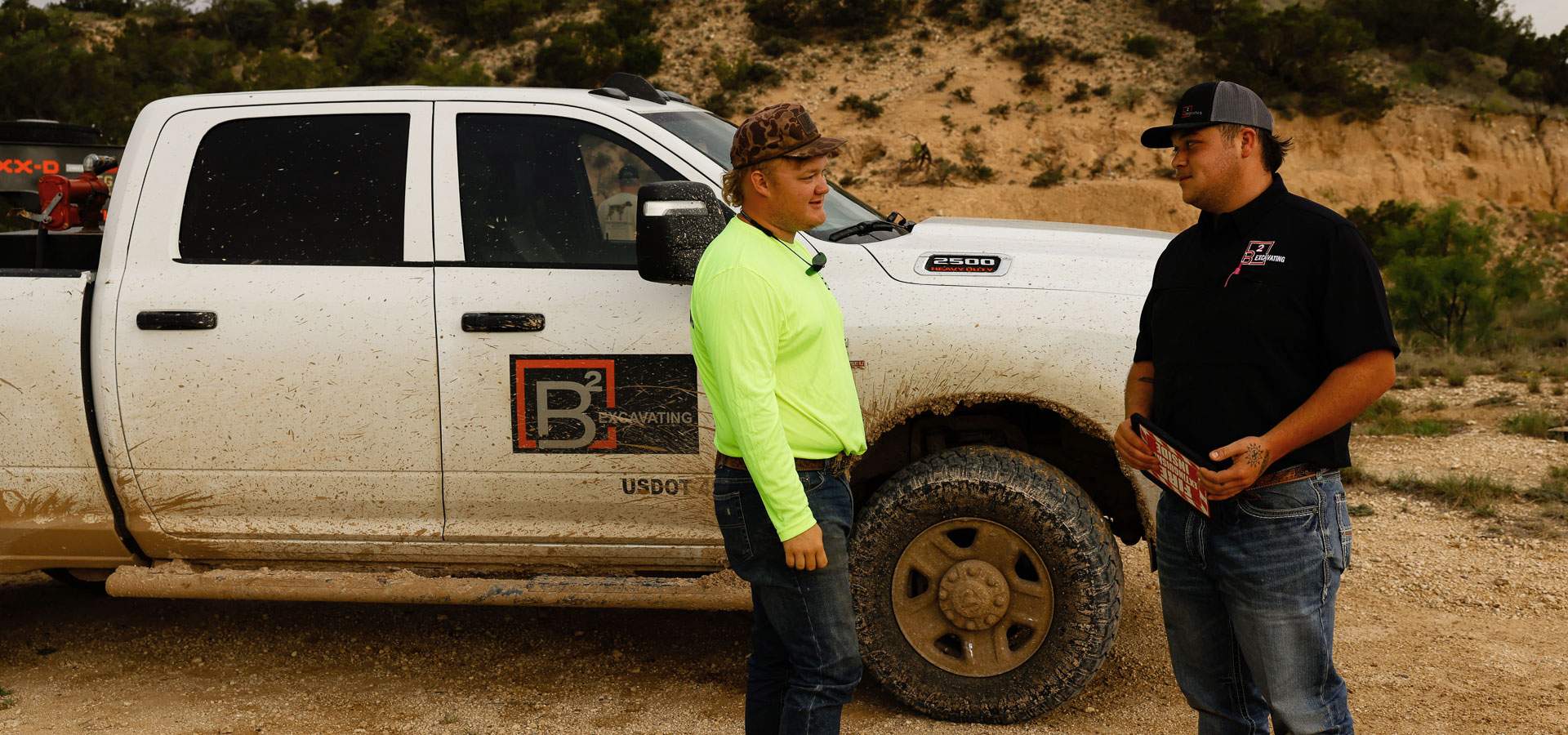 Two crew members in high-visibility gear talking beside a mud-covered crew-cab work truck on site