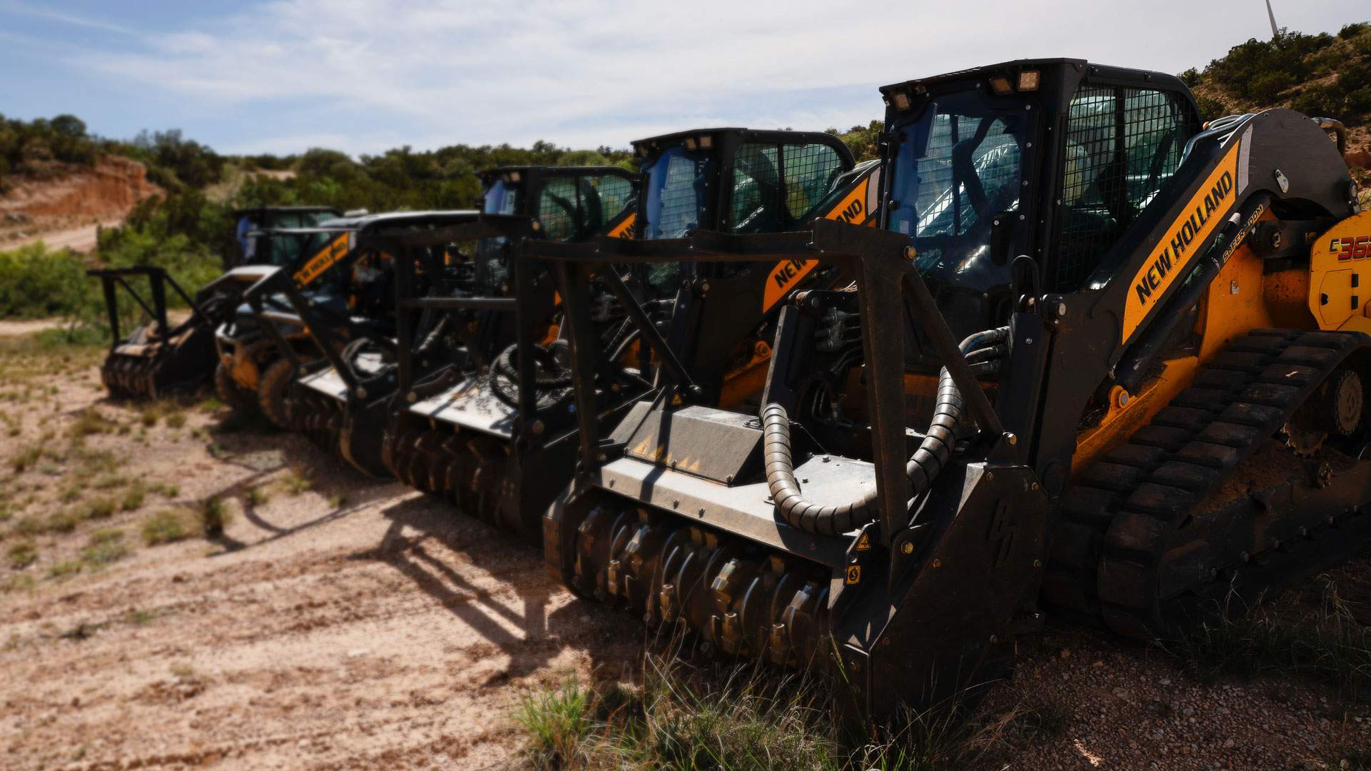 Row of New Holland compact track loaders fitted with drum mulching heads staged at a job site
