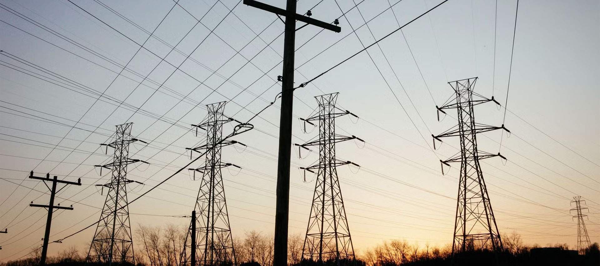 Transmission towers and conductors silhouetted at sunset along a maintained power line right-of-way